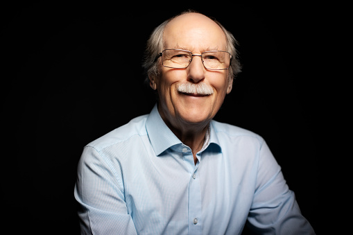 Portrait of a senior man looking happy against black background. Studio shot of retired male in shirt smiling at camera.