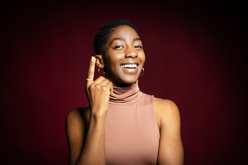 Beautiful african woman standing over dark background pointing finger up with successful idea. Exited and happy have an idea.