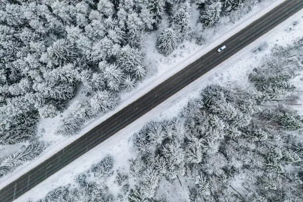 Photo of Aerial view of winter road with a car and snow covered forest in Finland