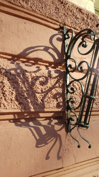 istock Elegant metal grating element on stucco wall with patterned shadows on beige plaster surface. Vintage ornate details of retro architecture building in Odessa Ukraine. 1199622195