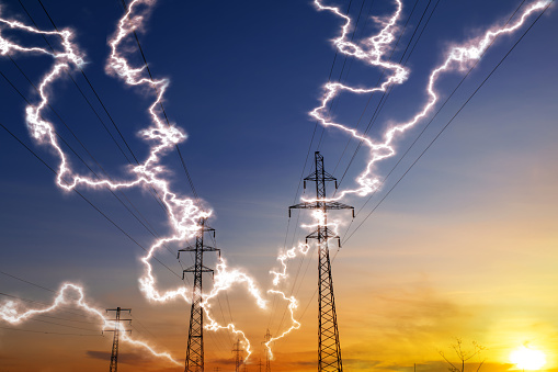 Power line against the setting sun with flashes of electricity discharges on wires. Concept of current flow through high voltage cables