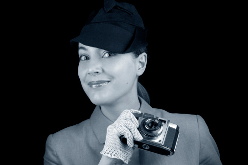 Young beautiful retro woman photographer with lace gloves and hat holding old camera. Toned.