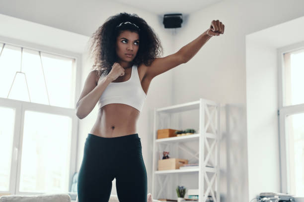 Strong young African woman Strong young African woman in sports clothing kickboxing while exercising at home kickboxing photos stock pictures, royalty-free photos & images
