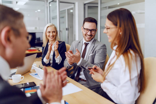 colleghi che applaudevano la loro collega per l'eccellente idea mentre erano seduti in sala riunioni. - dedizione foto e immagini stock