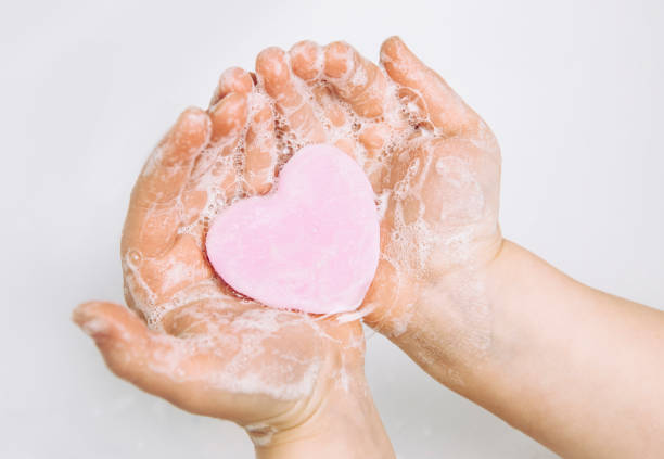 importance des soins d'hygiène personnelle. vue plate de laïc de l'enfant se lavant les mains sales avec la barre rose de savon de forme de coeur, beaucoup de mousse. copiez l'espace. - color image season people wet photos et images de collection