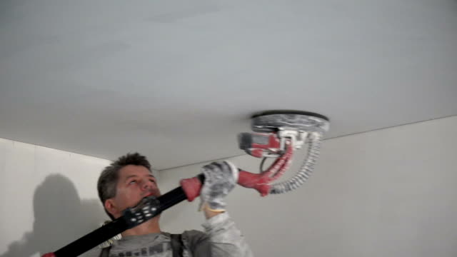 Male construction worker smoothing ceiling surface with sanding machine