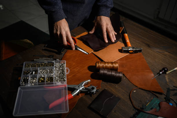 istock Leather goods master hands cutting piece of natural leather with crafting tool. Workflow in the workshop. 1199640095