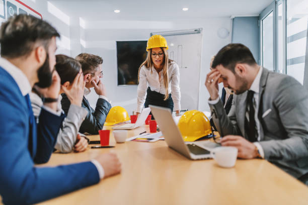 istock Attractive caucasian female architect leaning on table and looking at paperwork. Colleagues listening to her. There is a problem with project. 1199641964