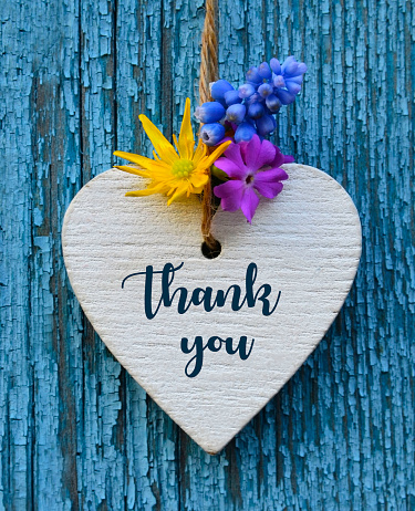 Thank You or thanks greeting card with flowers and decorative white heart on blue wooden background.\nInternational Thank You Day concept.Selective focus.
