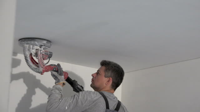 plasterer man smoothing ceiling with polishing sanding machine. House finishing