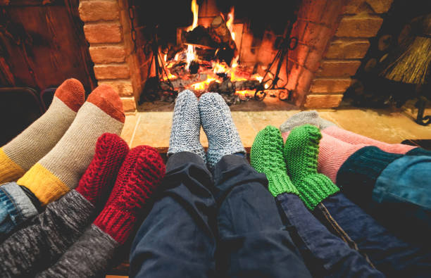 legs view of happy family wearing warm socks in front of fireplace - winter, love and cozy concept - focus on center grey woolen socks - fire place imagens e fotografias de stock