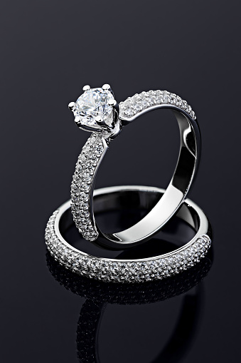 Female wedding diamonds rings on black background. Silver engagement rings with gemstone. Advertising jewelry still life
