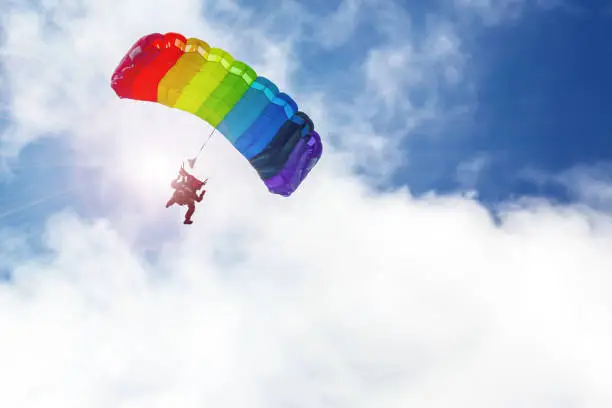 Photo of Skydiver flying on a parachute rainbow colors in the sun, against the sky.