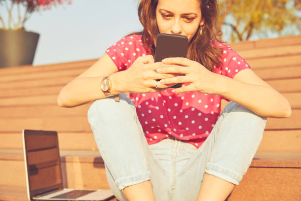 istock Attractive woman using cellphone while working on laptop outdoors. 1199650259