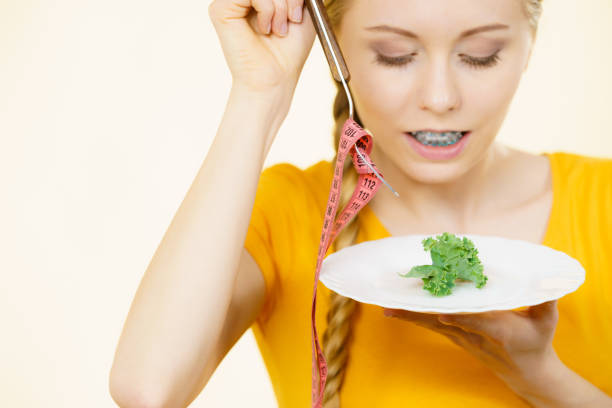 Happy young smiling woman about to eat lettuce holding plate and fork with tape measure.