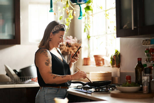 Recipe management made easier with mobile apps Shot of a young woman using a smartphone while preparing a meal at home woman making healthy dinner stock pictures, royalty-free photos & images