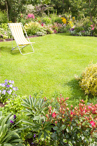 Garden chair on a green lawn in a beautiful flower garden in summer, vertical