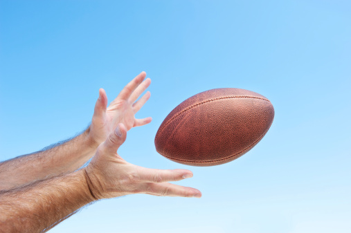 A football player catches a spiral pass.  Clear sky good area for placing copy.