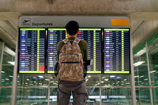 istock Young man with backpack looking at blurry flight information display screen at the airport 1199651912