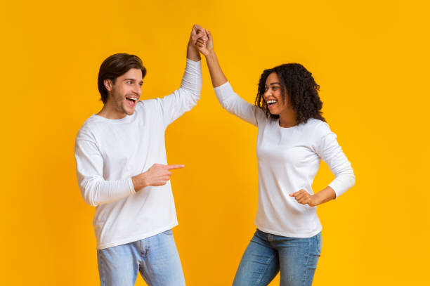 istock Affectionate interracial couple holding hands and dancing together over yellow background 1199661059