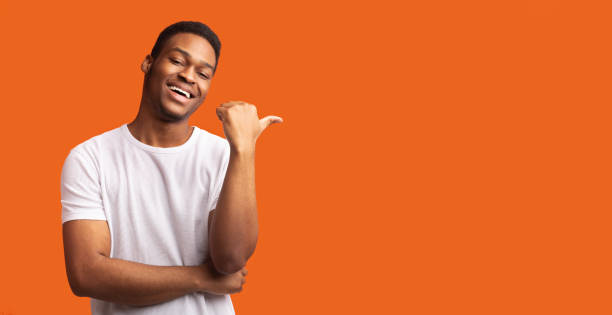istock Young afro guy pointing at copy space with thumb up 1199663463
