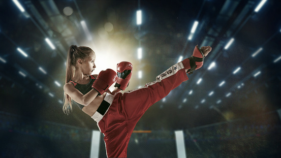 Confident. Young female kickboxing fighter training in the gym. Caucasian blonde girl in red sportswear practicing in martial arts. Concept of sport, healthy lifestyle, motion, action, youth.