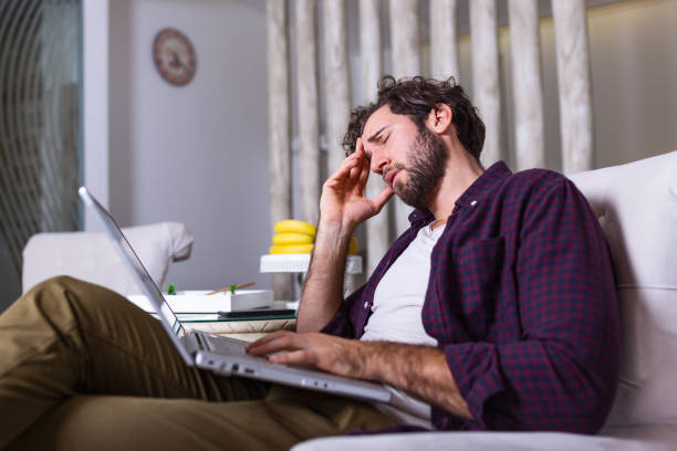 istock Young tired manager sitting at home surrounded with papers and laptop computer having tired look holding his hand on head having pain closing his eyes being sleepy and exhausted. Tiredness 1199665128