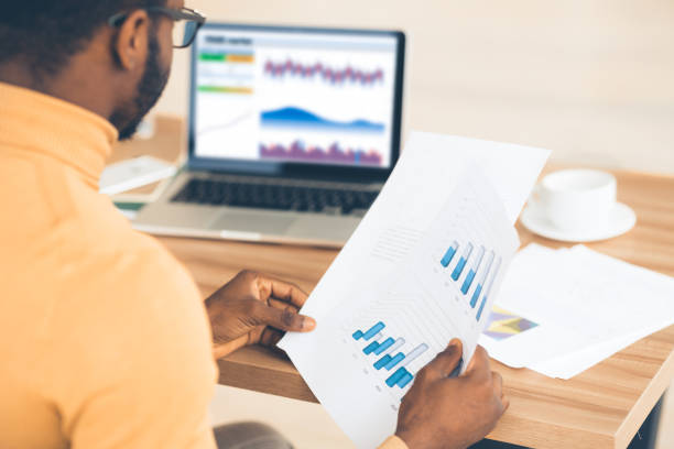 istock Black manager working with diagrams on pc and paper 1199665335