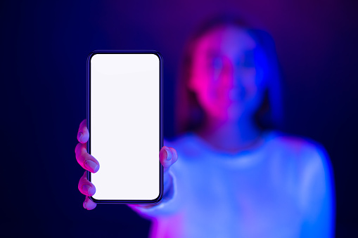 Cool app. Girl showing phone with blank screen in neon lights, free space