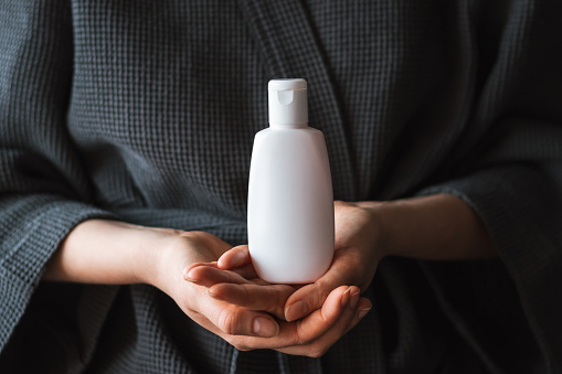 White cosmetic bottle in a female hands. Branding mock-up.