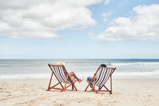 Shot of a young couple relaxing on their chairs at the beach