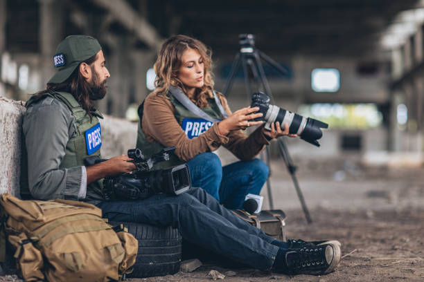 Man and woman, war journalist with cameras at the place of action in war zone, taking a break.