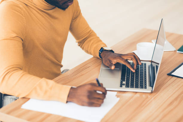 istock Unrecognizable afro guy working on his laptop and writing 1199671950