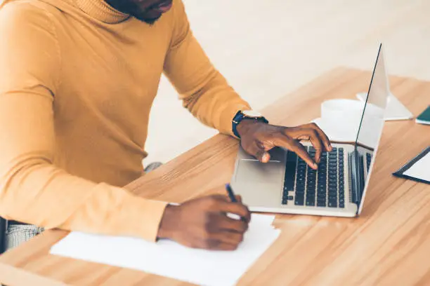 Photo of Unrecognizable afro guy working on his laptop and writing