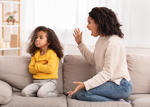 Angry Afro Mother Shouting At Offended Daughter Sitting On Couch At Home. Family Problems, Quarrels And Aggression
