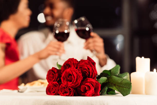rosas tumbadas sobre la mesa, cónyuges irreconocibles bebiendo vino en el restaurante - valentines day fotografías e imágenes de stock