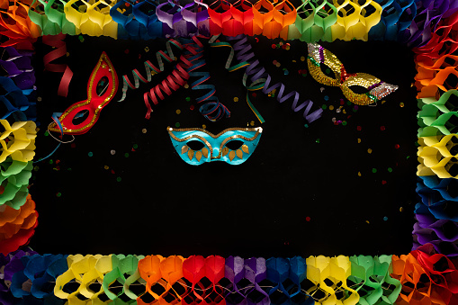 Carnival objects on a black background with colourful border. Coiled streamers, masks, confetti, and many other carnival objects