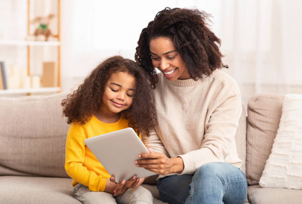 istock Mother And Daughter Using Tablet Sitting On Sofa At Home 1199676542