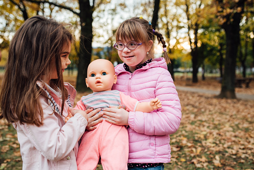 Little girl with Down syndrome and her sister playing with a doll in the park.