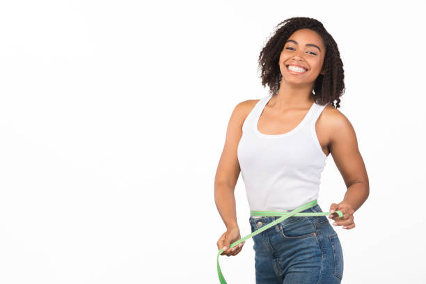 Portrait of young black girl measuring waist Weight Loss. Happy afro woman measuring her waist using tape after fitness exercise, smiling at camera. Free space fat nutrient photos stock pictures, royalty-free photos & images