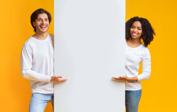 istock Cheerful Guy And Afro Girl Pointing At White Advertisement Board 1199678154