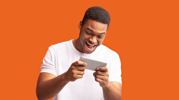 istock Excited afro man using mobile phone on orange background 1199678215