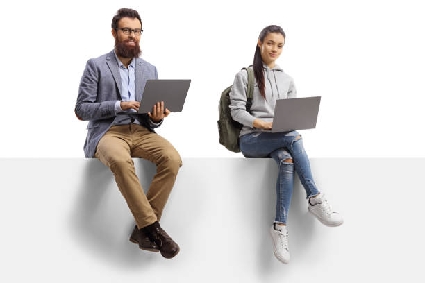 istock Female student and a bearded man sitting on a blank board and using laptop computers 1199678318