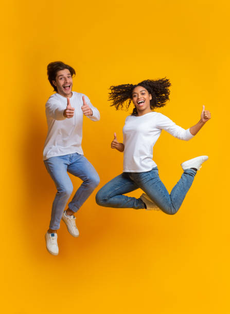 istock Excited Multiracial Couple Jumping And Gesturing Thumbs Up, Having Fun Together 1199678429