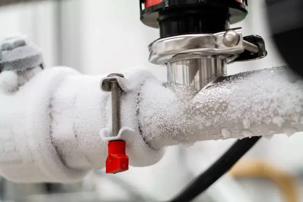 Photo of Frozen liquid nitrogen carrying pipes with a valve and black plastic lever close up in a science laboratory