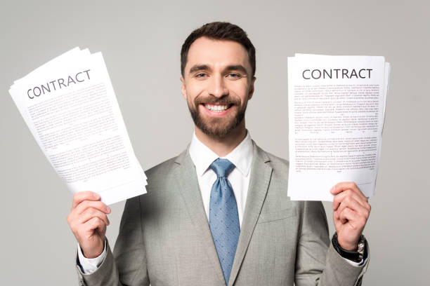 istock happy businessman holding contracts and looking at camera isolated on grey 1199678728