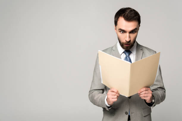 istock shocked businessman looking at documents in paper folder isolated on grey 1199678776