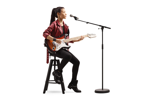 Young woman playing a guitar and singing on a microphone isolated on white background