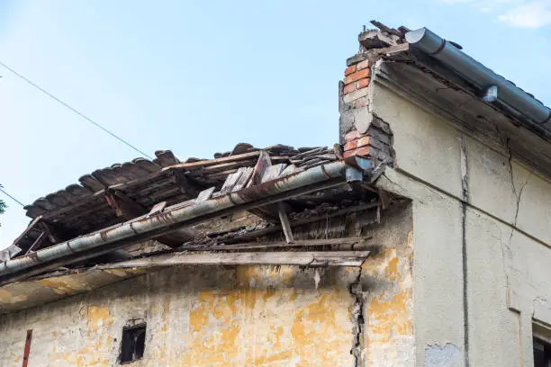 Photo of Remains of hurricane or earthquake aftermath disaster damage on ruined old houses with collapsed roof and wall with dust in the air