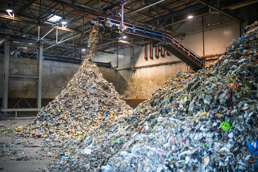 Floor-level action shot of separated recyclables falling from elevated conveyor belt onto growing pile inside waste management facility.